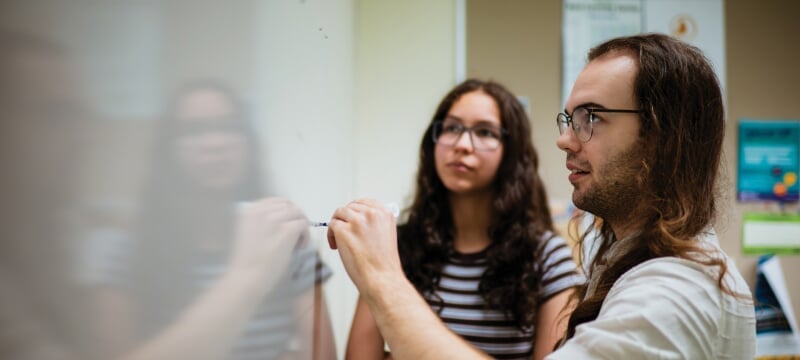 Two students writing on a whiteboard.