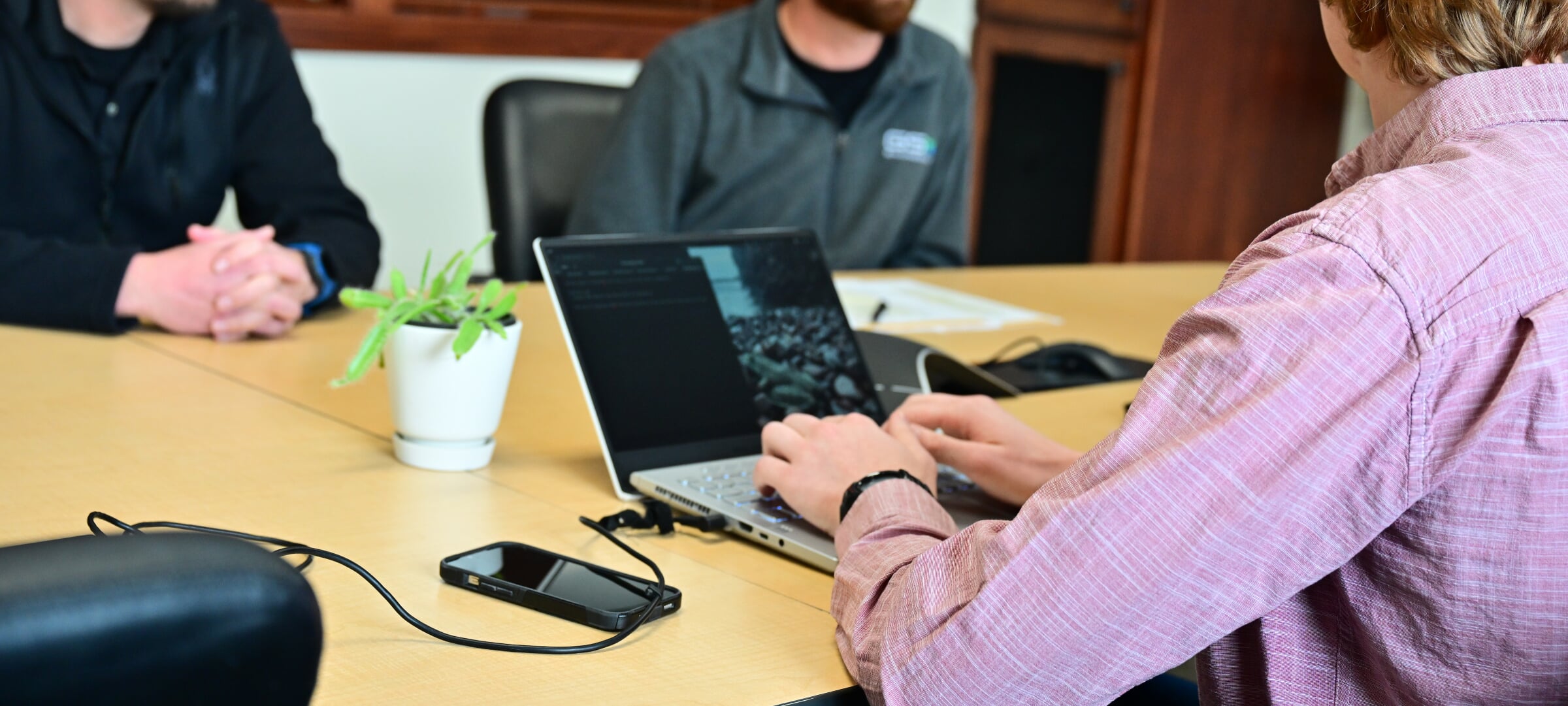 Students sit around a table. One types code on a laptop.