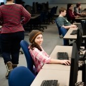 Young students sitting at computers while an instructor walks behind them