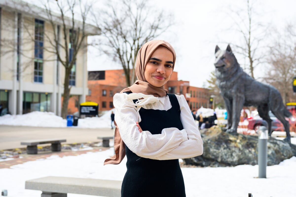 A Michigan Tech data science graduate stands in front of the Husky statue on a snowy spring day in Houghton, Michigan.