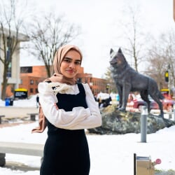A Michigan Tech data science graduate stands in front of the Husky statue on a snowy spring day in Houghton, Michigan.