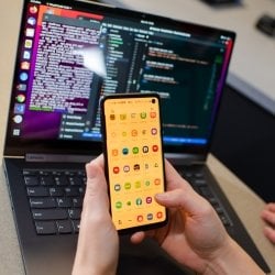 Hands holding a cell phone in front of a laptop.