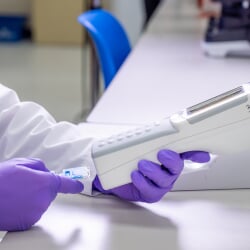 Gloved hands insert a sample into a handheald machine for reading.