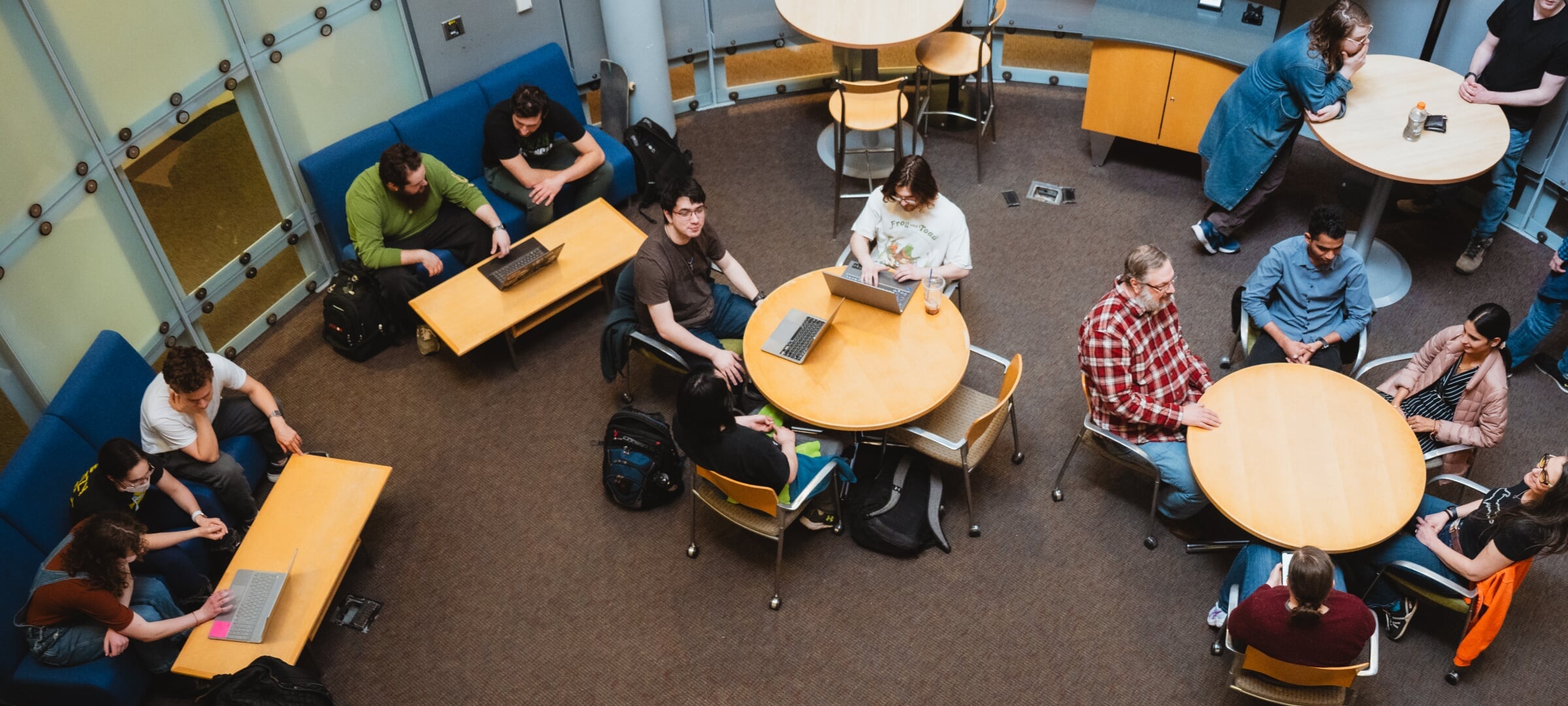Data science students at various tables discussing work on laptops.