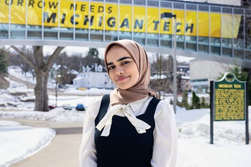 Tabasum Hamdard, a young woman in a hijab, in front of the Tomorrow Needs Michigan Tech skywalk.
