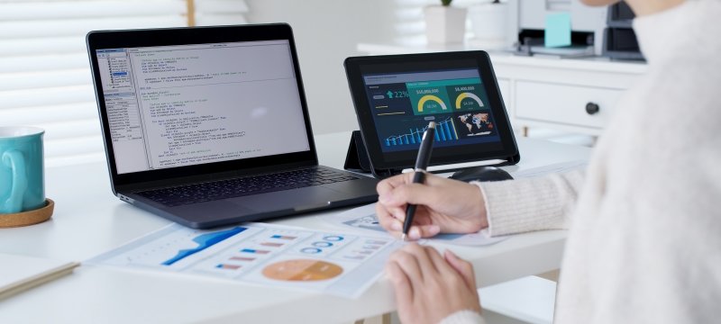 student working on a desk with data on several computer screens and papers on the desk