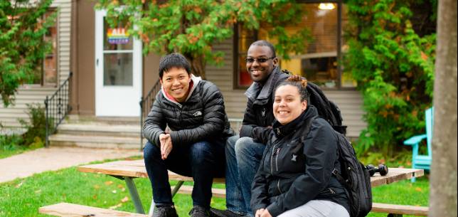 Three Husky Connect Students sitting outside the Center for Diversity and Inclusion smiling. 