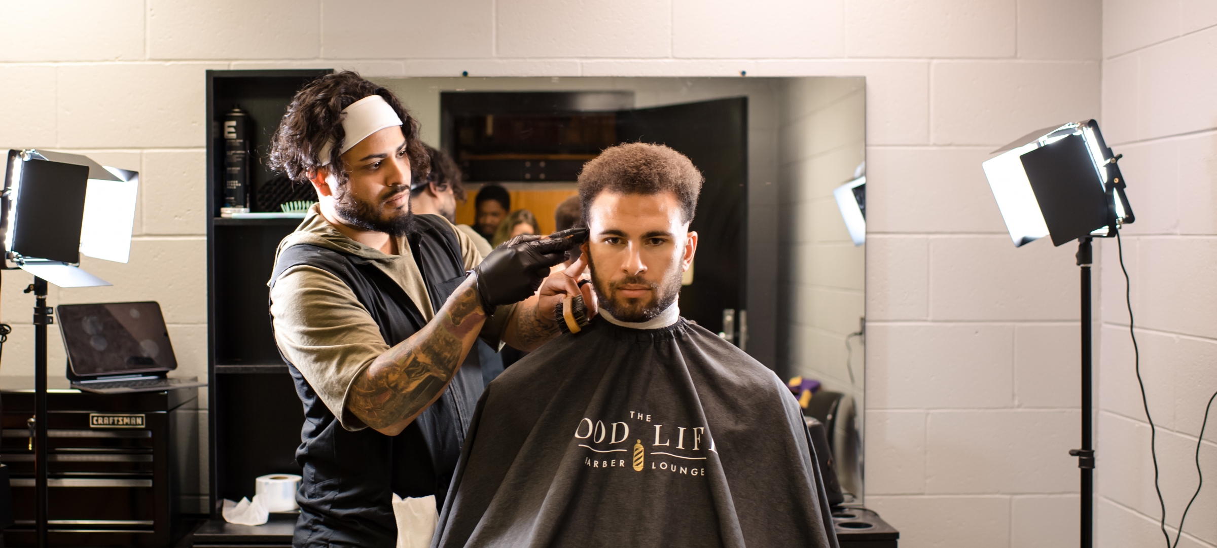 A barber cuts the hair of a non-white student with textured hair.
