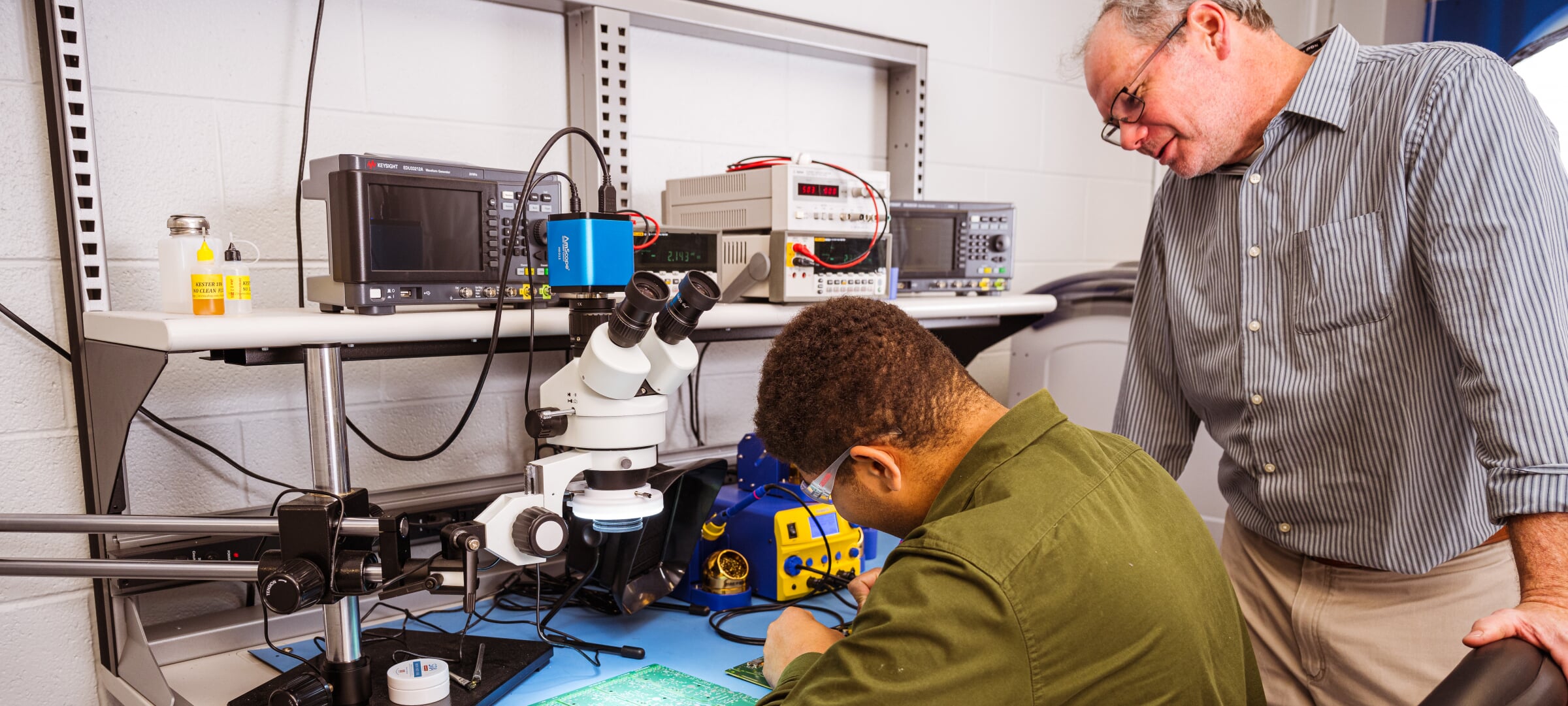 A student being mentored while working on a circuit board