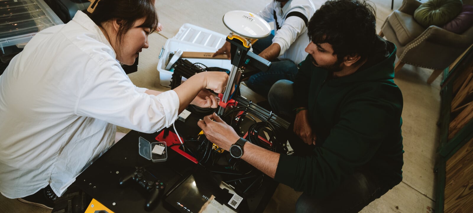 Three students work on the interior of a medium-sized wheeled robot.