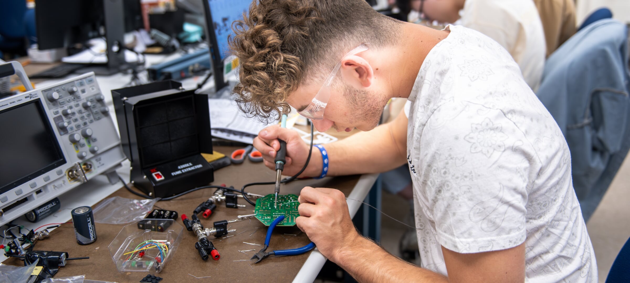 Student soddering a wire onto a circuit board.