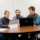 Three students sitting at a table with computers.