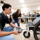 Students holding a remote control for a robot.