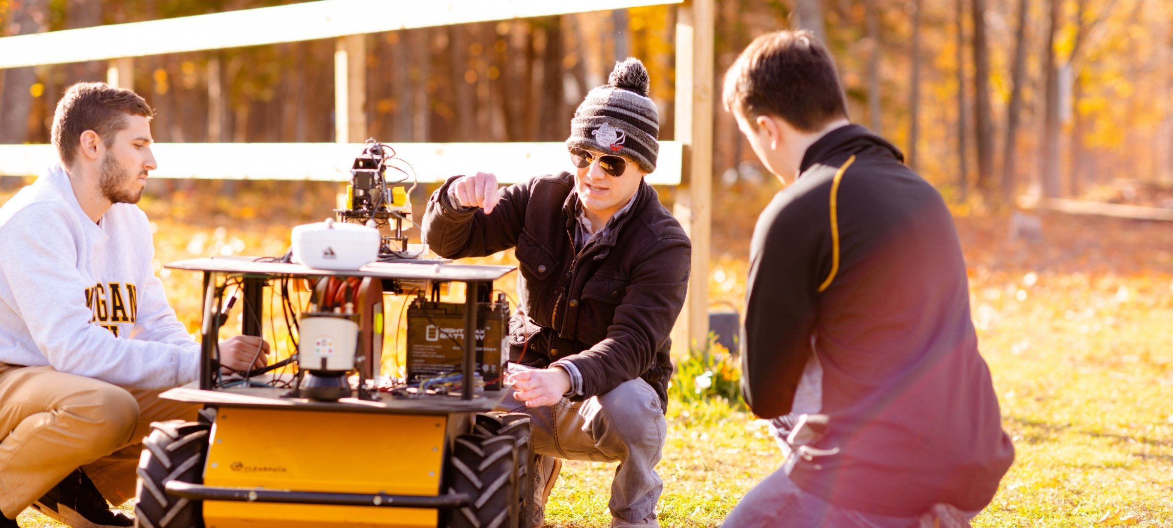 Professor and two students outside looking at a robot.