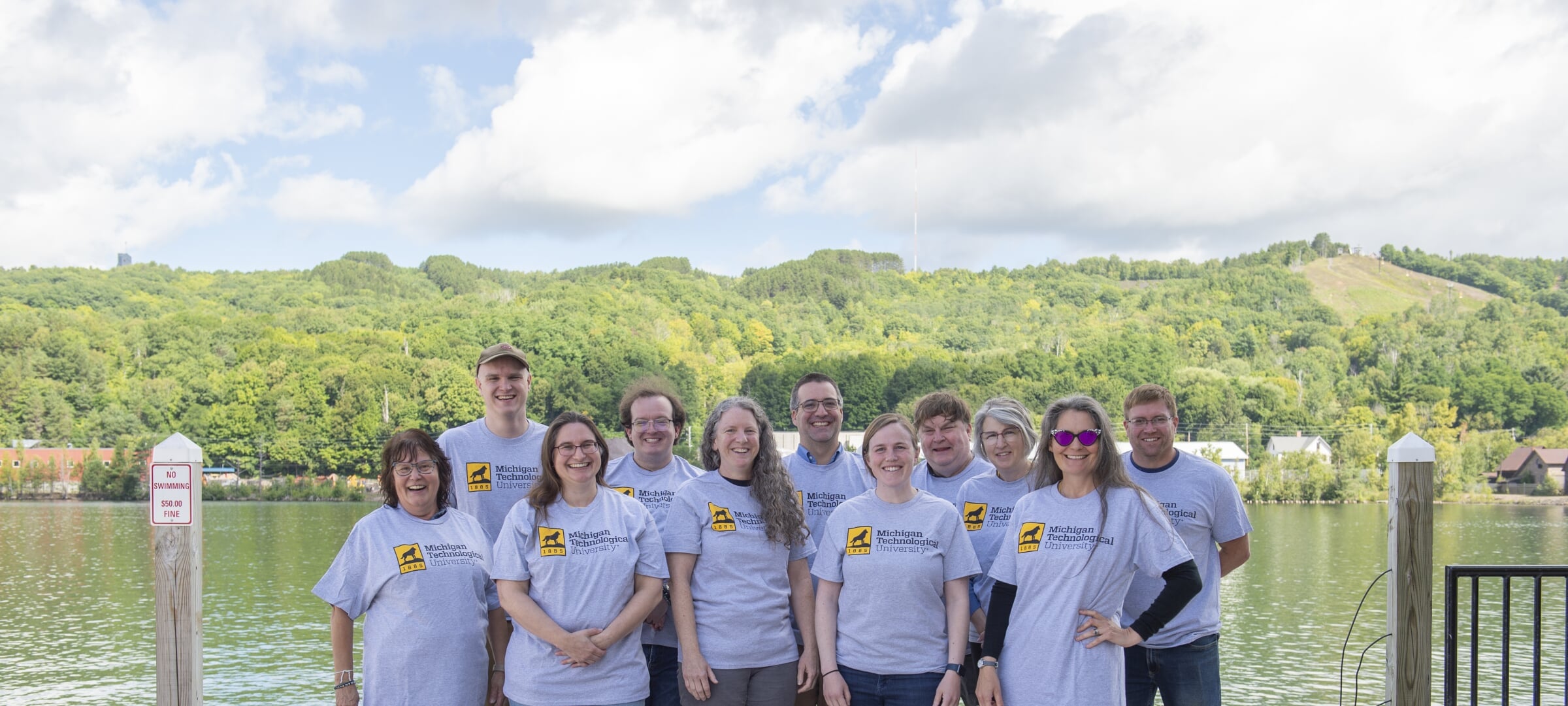 Eleven engineering fundamentals faculty and staff pose with MTUengineering T-shirts in front of the Keweenaw Waterway.