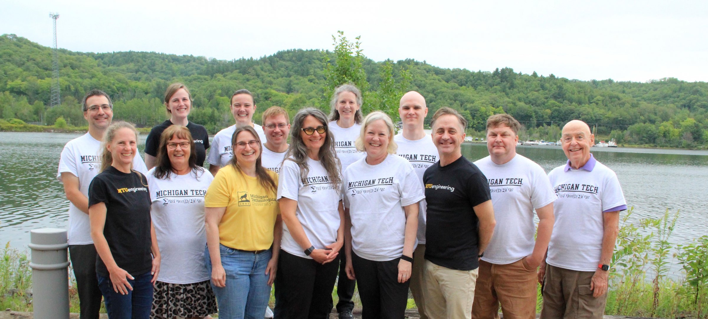 Fourteen engineering fundamentals faculty and staff pose with MTUengineering T-shirts in front of the Keweenaw Waterway..