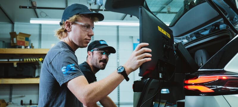 two individuals using a monitor behind a car inside a building