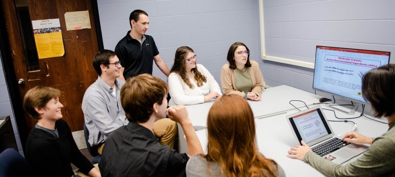 Engineering students and faculty around a monitor at a table.