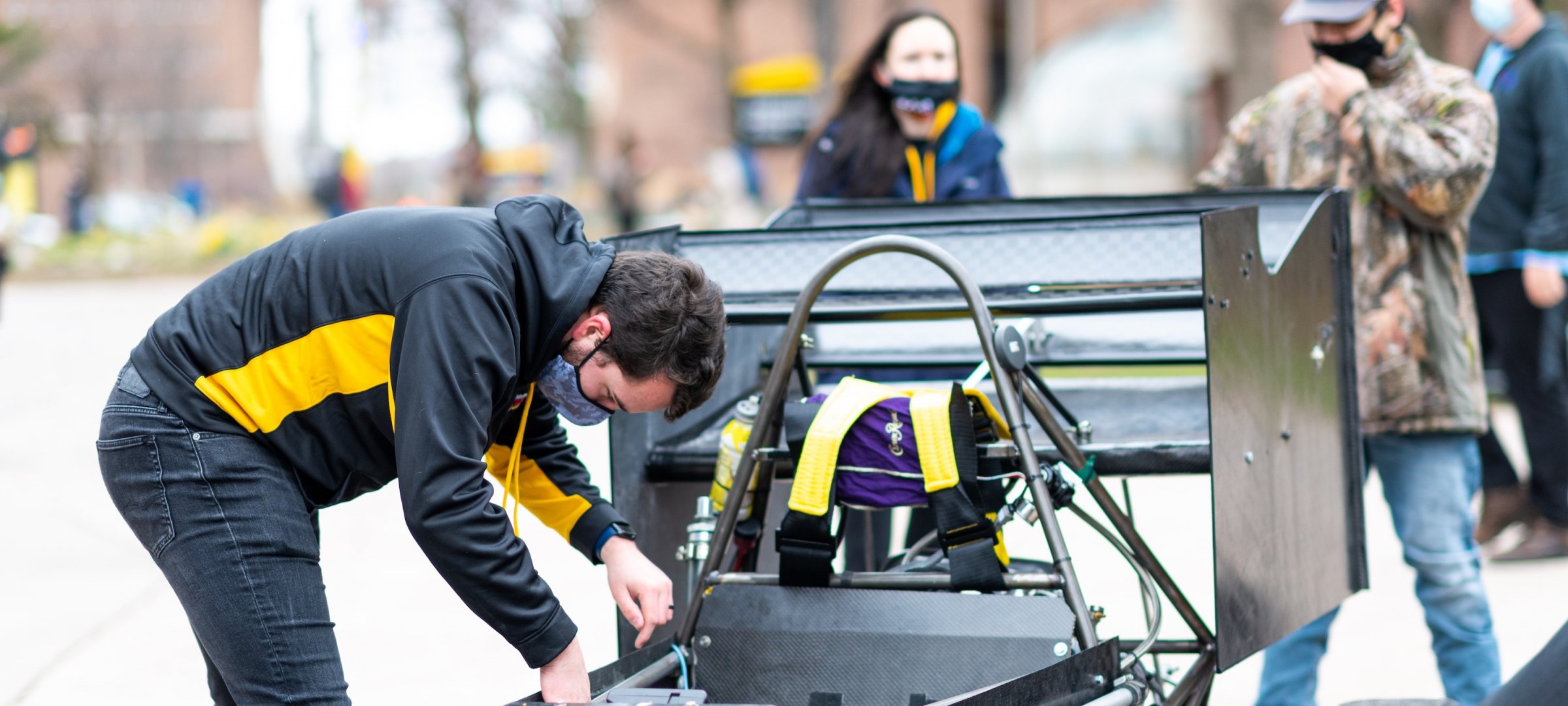 Students outside in the snow examining a race car.