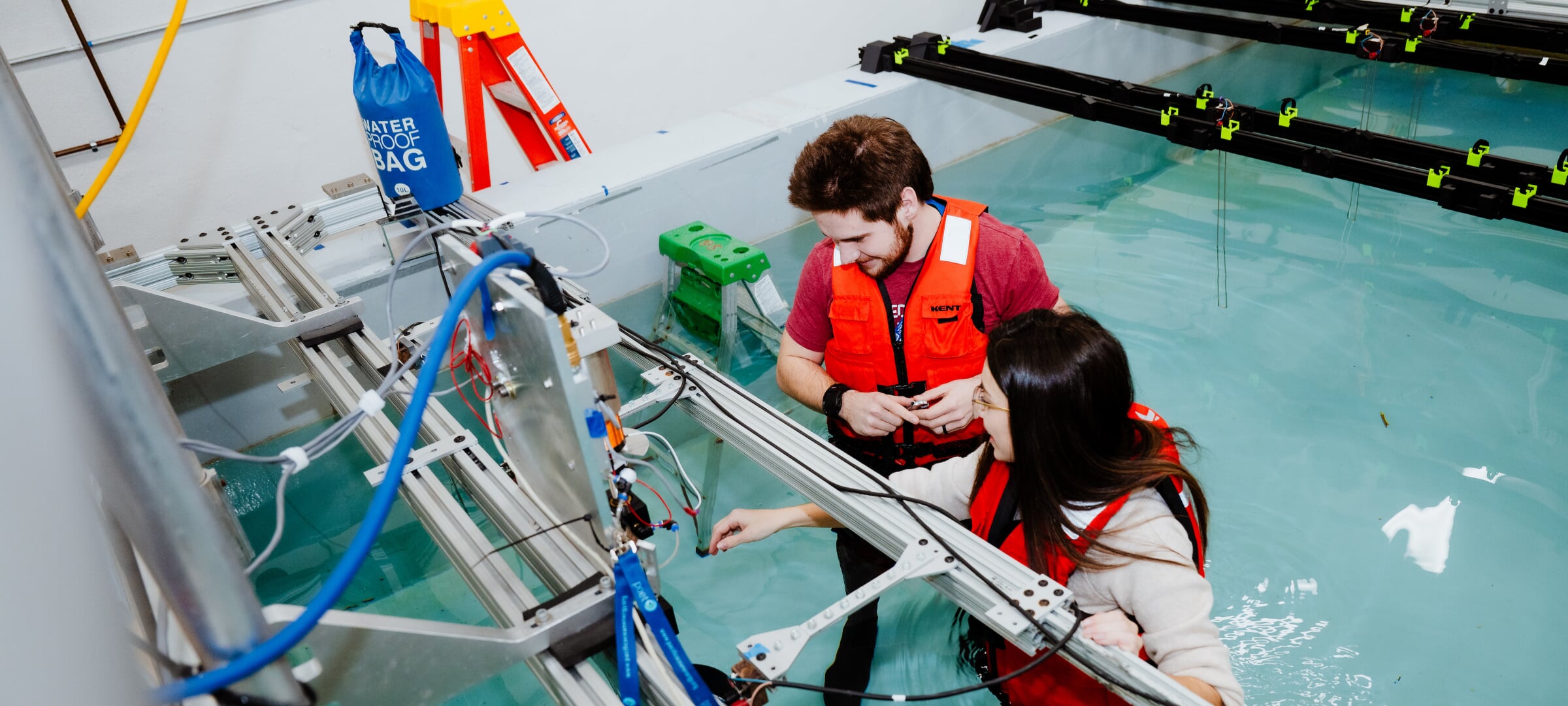 Two student researchers standing in a wave tank lab looking at equipment