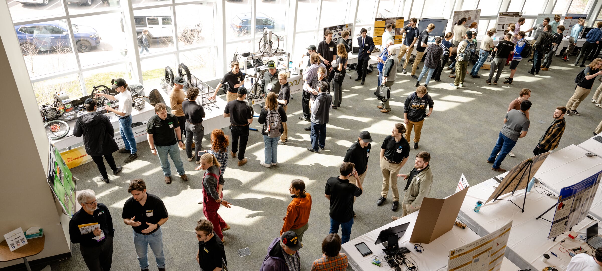 Design Expo — view of the design expo featuring students standing next to their displays setup on tables in rows