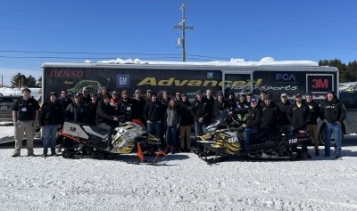 Clean Snowmobile Challenge Team and snowmobiles in front of the team trailer outdoors