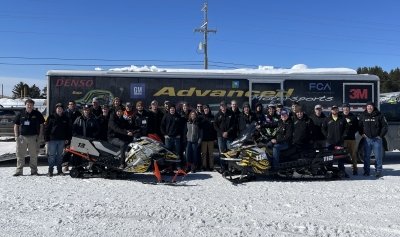 Clean Snowmobile Challenge Team and snowmobiles in front of the team trailer outdoors