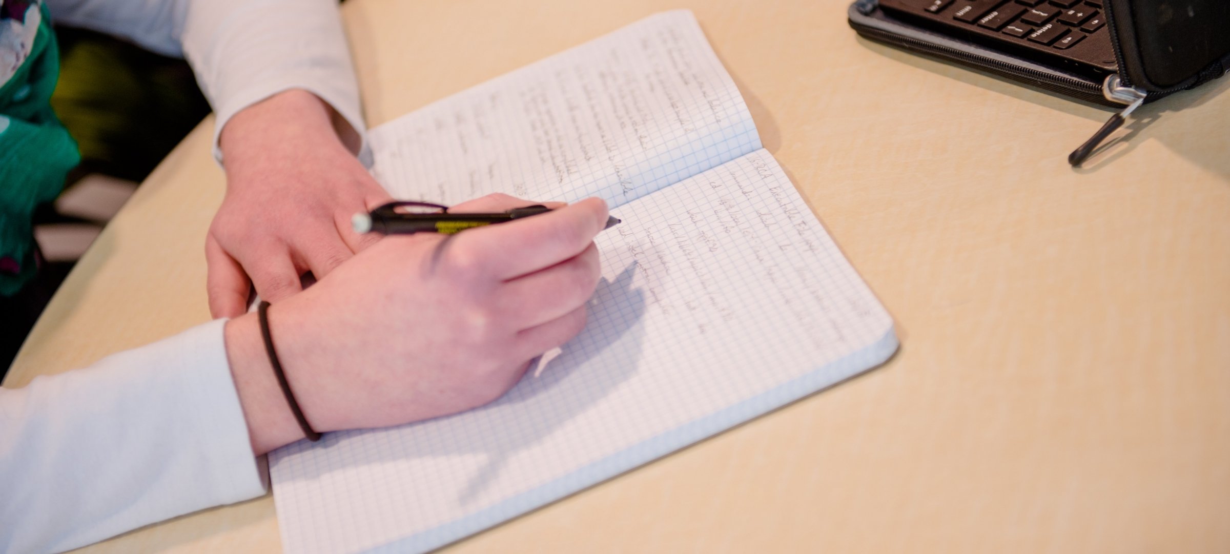 Someone writing in a journal next to a laptop