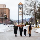 four students walking through campus in winter with a clocktower in the back
