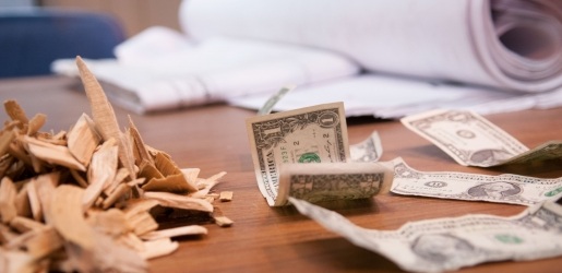 Photo of dollar bills, wood chips, and paper shown on a wooden table.