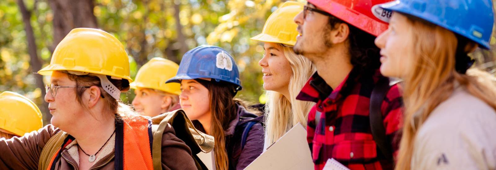 Students in a forest, wearing hard hats.