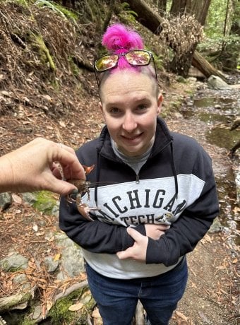 Krause with an invasive rusty crayfish being held in front of them making a face that says yikes