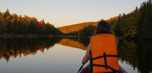 Girl paddling a canoe on still water with forest in the background.