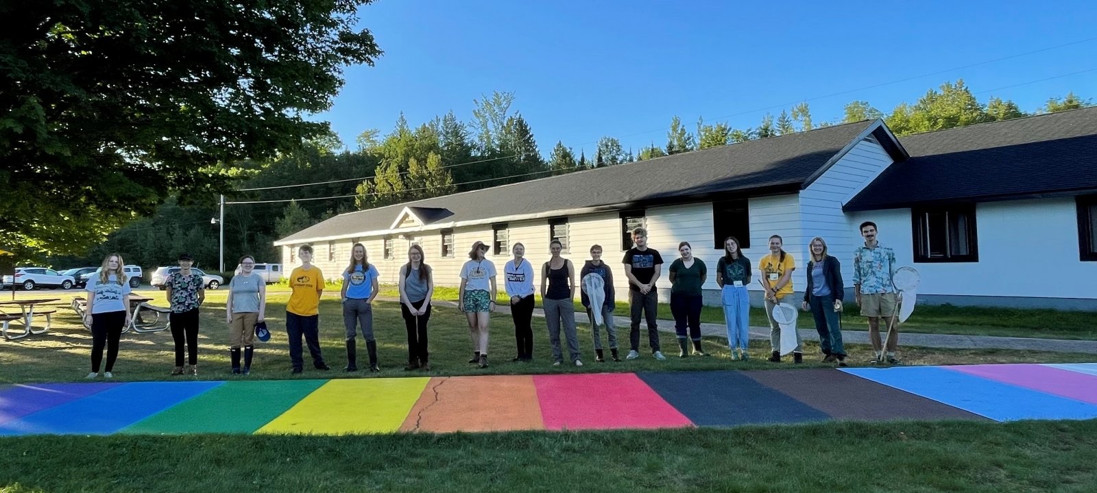 Students standing behind a progress pride flag painted on a sidewalk at the Ford Center.