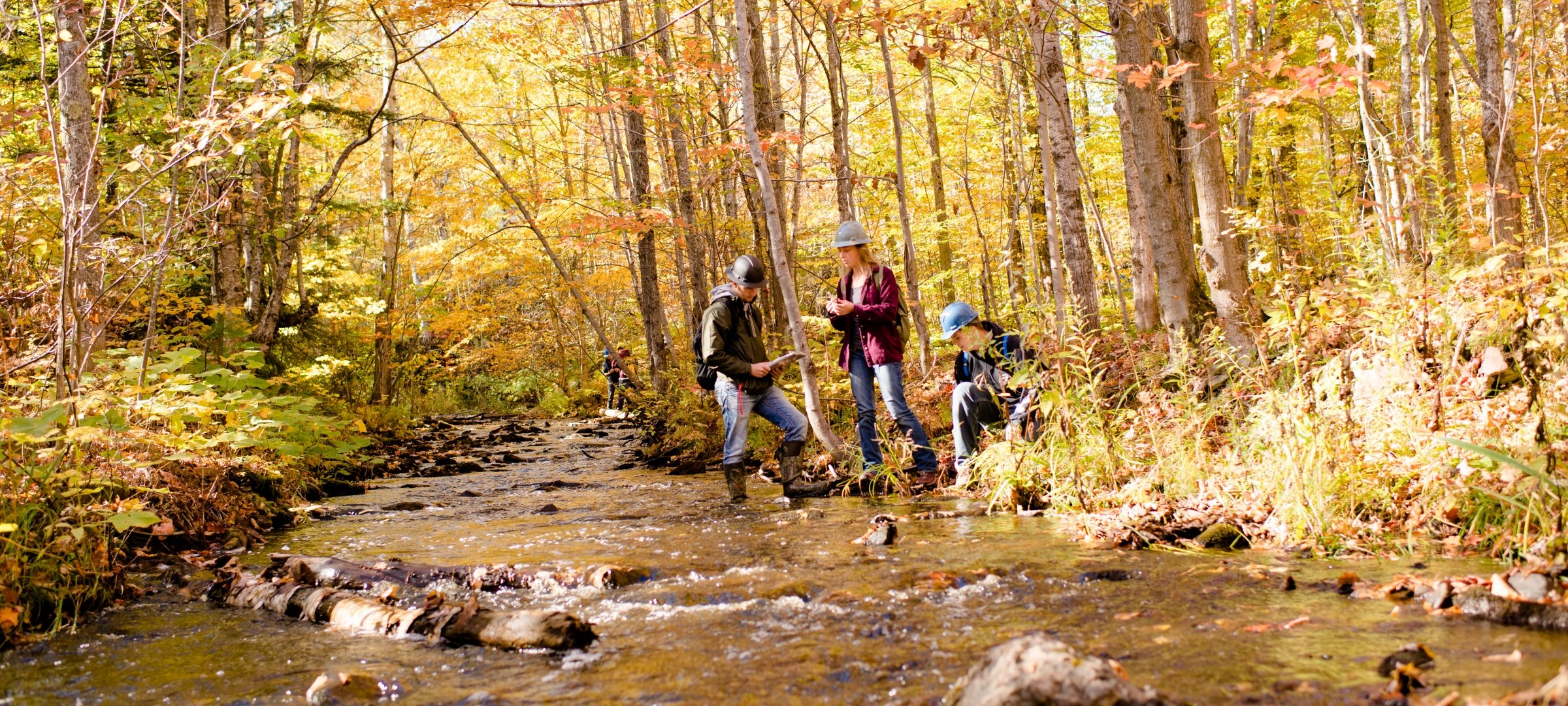 Three graduate students with hard hats standing in a stream taking samples.