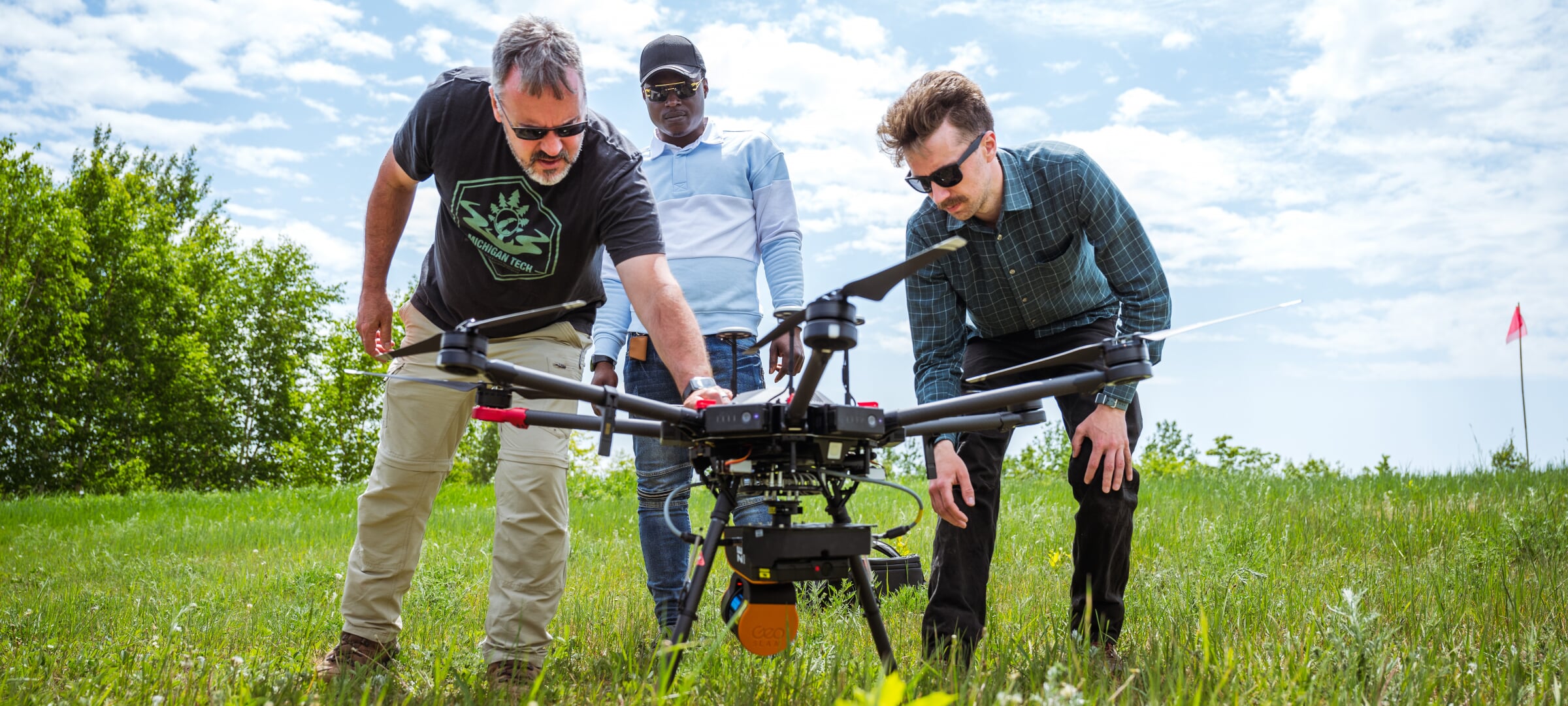 Three people in a grassy area working with a large 8-armed drone
