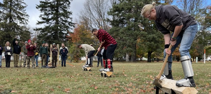 Three people stand on logs on stands chopping while spectators look on as Society of American Foresters Forestry Club students from Michigan Tech and other colleges compete.