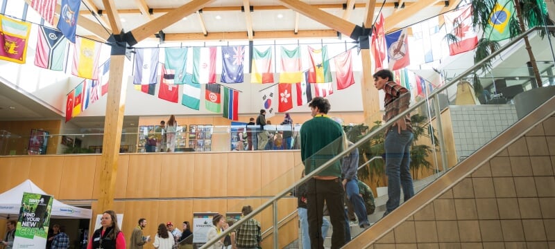 Students meeting with companies during the career fair in the Atrium with international flags hanging.