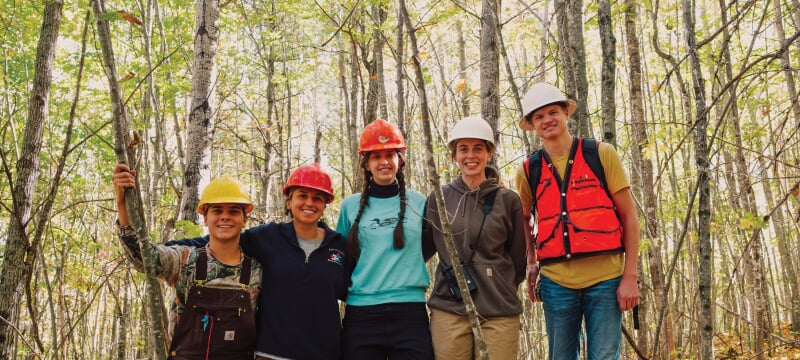 Students wearing hard hats standing together in the woods.
