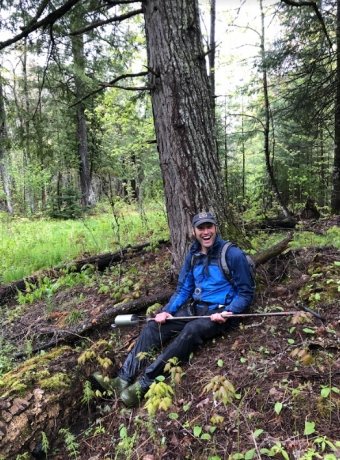 Luke Nave sitting on the forest floor while holding a tool