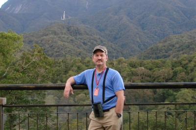 Tom standing on a deck overlooking trees and mountains