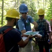 Students in hard hats working on a project in the woods.