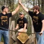 Three forestry students sawing a large log and high fiving