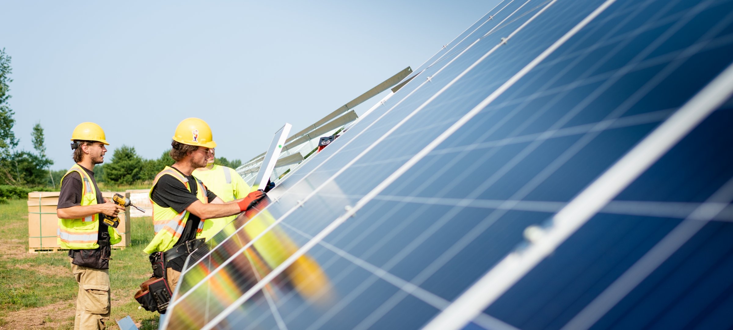 Two students with hard hats and work vests working on a large solar panel