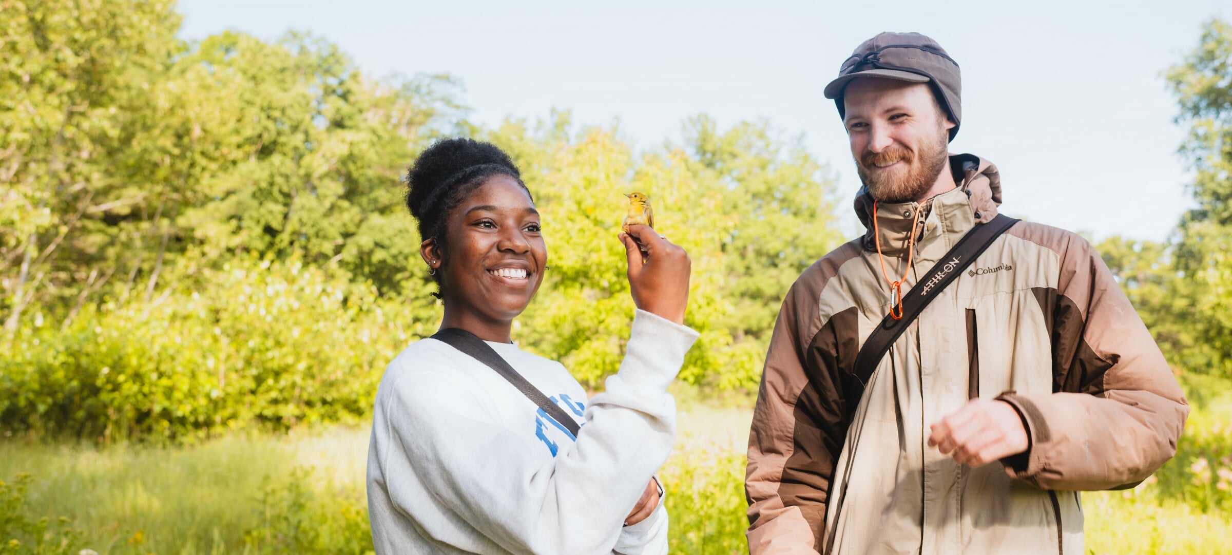 A bird perches on a student's hand while another looks on and smiles.