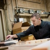 Person sitting at a lab desk reaching for a piece of wood