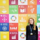Student standing in front of a colorful background with logos and colorwheels