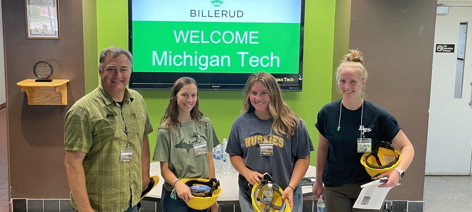 Students and instructor holding hard hats. Tv In background says "Welcome, Michigan Tech"