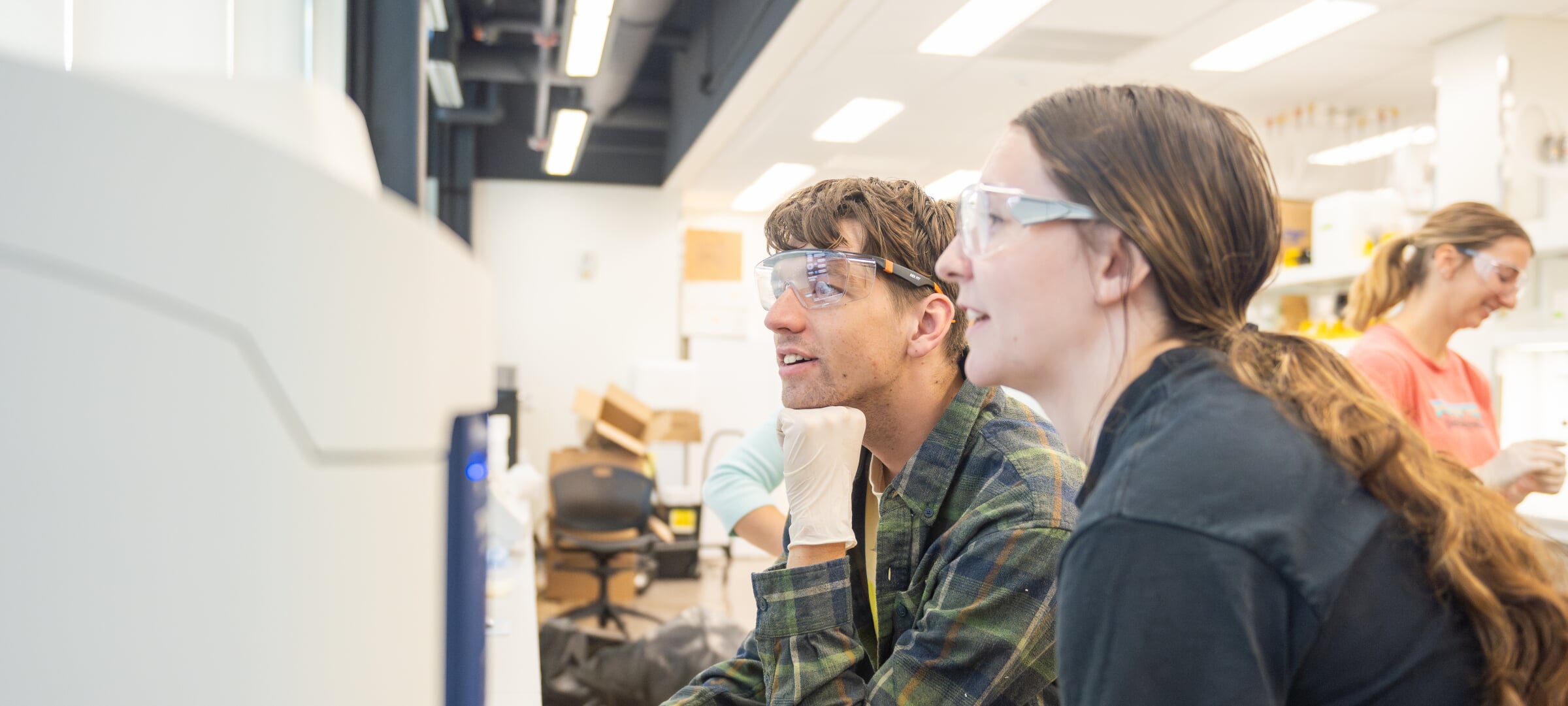 Two students with safety glasses in a lab monitoring.
