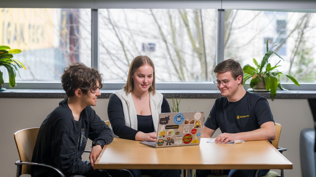 Three students sitting looking at a laptop.